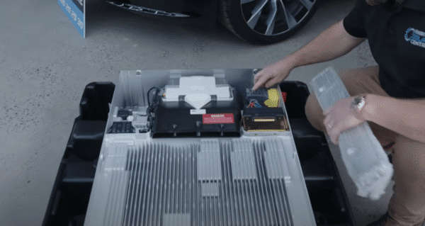 A person examines a disassembled electric vehicle battery pack with various components visible.